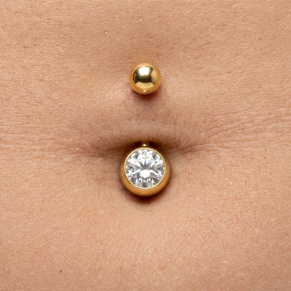 Goldenes Bauchnabelpiercing mit funkelndem Kristallstein auf Haut in Nahaufnahme