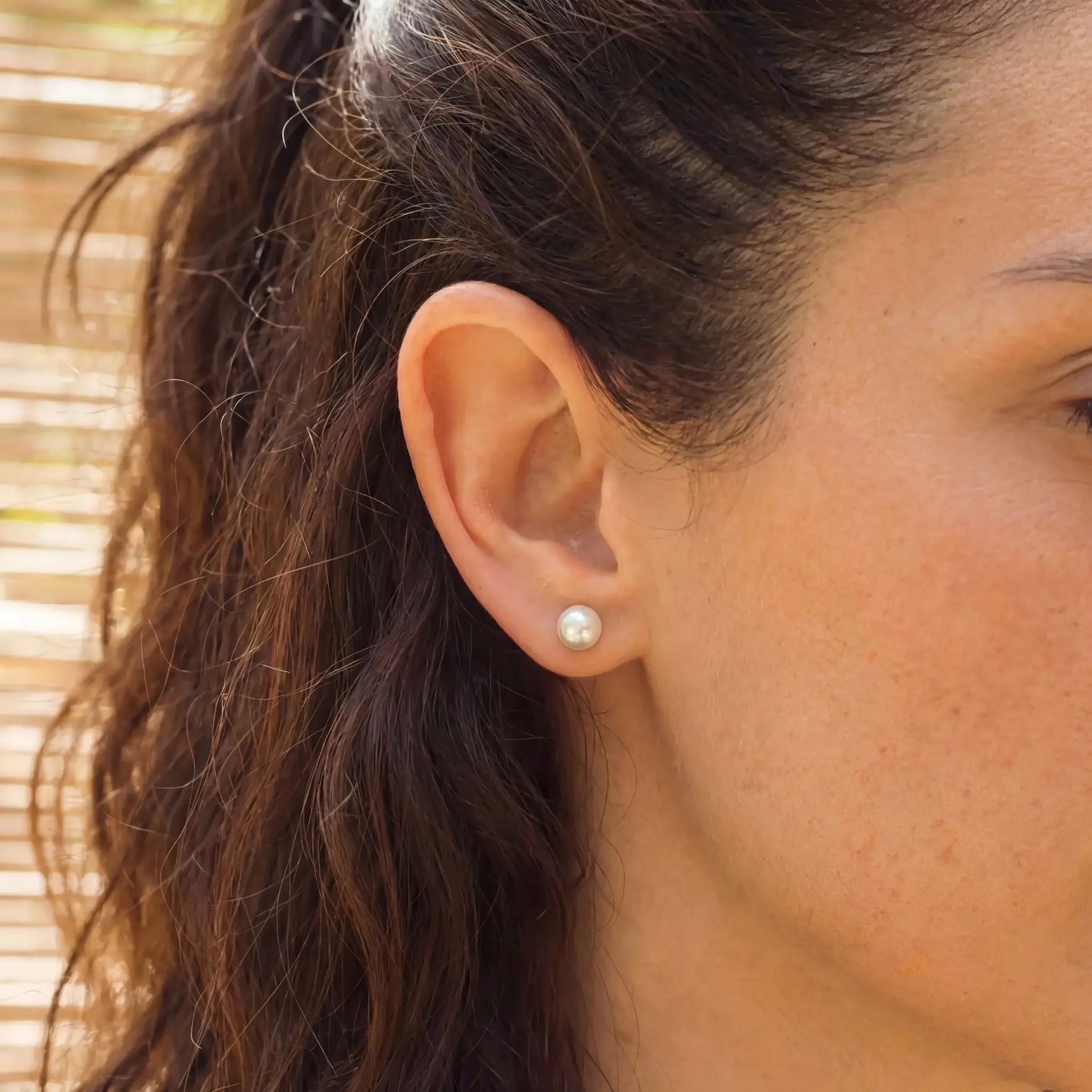 Seitliche Nahaufnahme eines Ohres mit Perlenstecker im Ohrläppchen