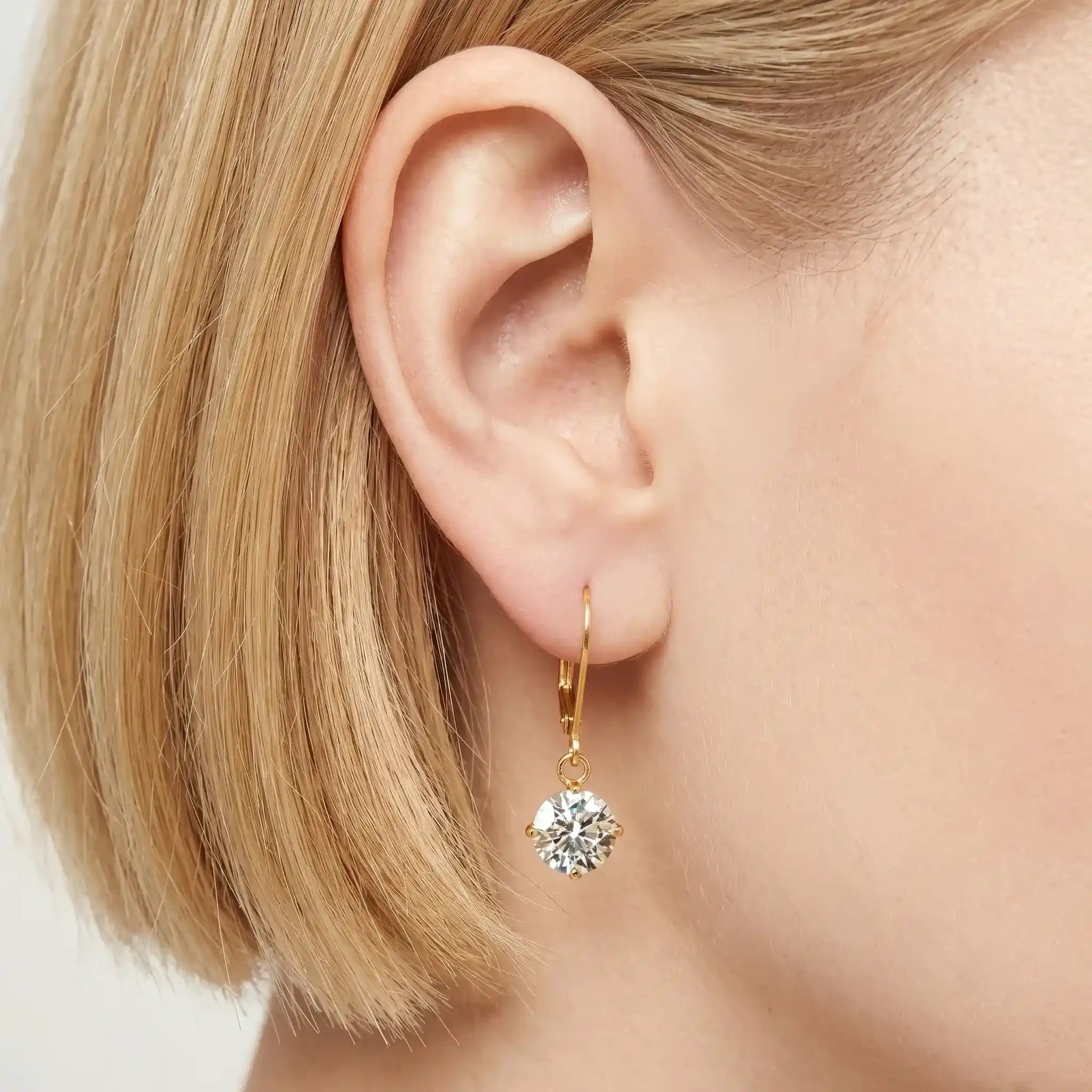 Goldfarbener Ohrring mit rundem klaren Stein am Ohr getragen, eleganter minimalistischer Schmuck